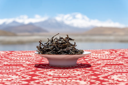 Dry tea leaves in a bowl on a red tablecloth with mountains in the backgroundの写真素材