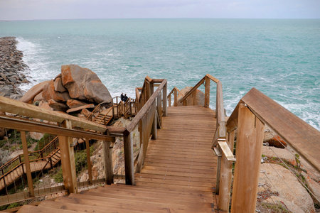 Wooden boardwalk leading down to a rocky coastline with turquoise ocean waves.