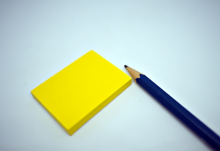 Yellow sticky note with blue pencil lying on the isolated white background