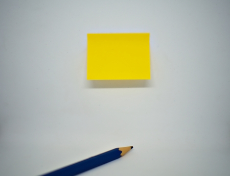A yellow sticky note on the wall with pencil lying on the isolated white backgroundの写真素材
