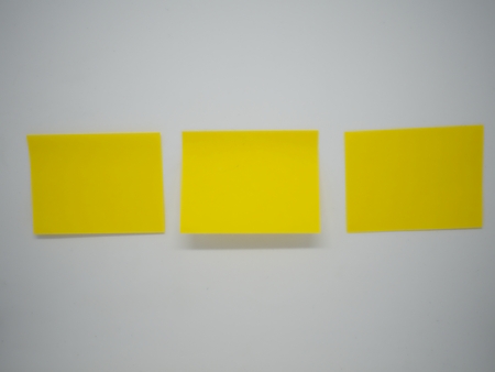 Three yellow sticky note stick horizontally on the white isolated wallの写真素材