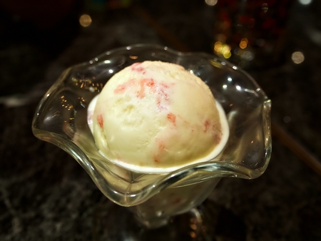 A scoop of straberry cheese cake ice-cream in the glass with black table under the spot lightの写真素材