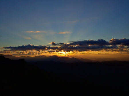 The wide landscape of the flare of the sun emerging from the sky and silhoette mountainの写真素材