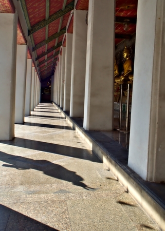 Thai style Buddist Temple corridors with the Buddha statue and the light and shadow of the shining sunの写真素材