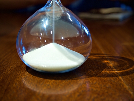The white sand watch on the table with dropping sand and the shadow