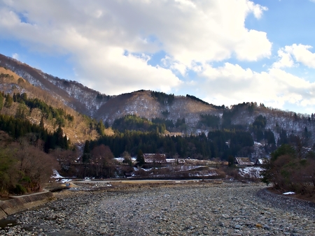 The landscape shot of Shirakawago from the bridge with melt mountain background and sky with cloud during Spring in Japanの写真素材