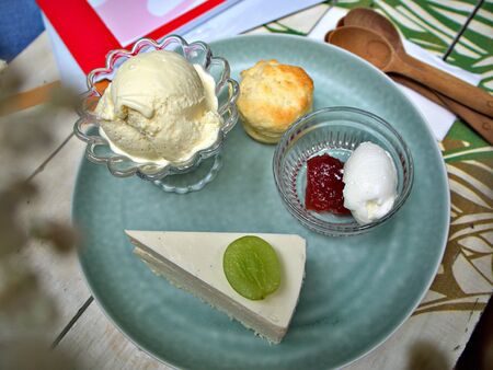 A plate of scone, ice-cream and a slice of green cheese grape cake on the plate with wooden spoon on the tableの写真素材