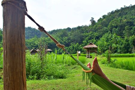 Side shot of the chilling leg on the cradle with cottage and green mountain background Chiang Mai, Thailandの写真素材