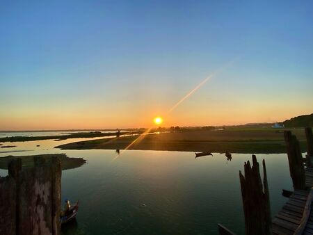 Sun set over the lake with flare in U-Being Bridge, the longest teak bridge of the world in Mandalay, Myanmarの写真素材