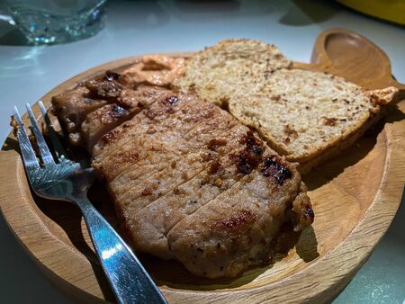 The pork steak with saue and grilled bread as appetizer on the wooden plate with forkの写真素材