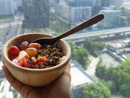 A bowl of yogurt wiht fruit and oat meal on the palm of hand with blur city backgroundの写真素材