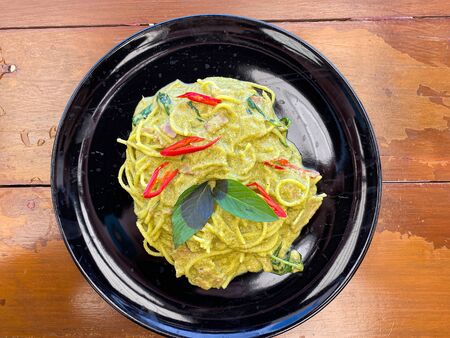 The Thai style green curry spagetthi on the black plate with wooden table backgroundの写真素材