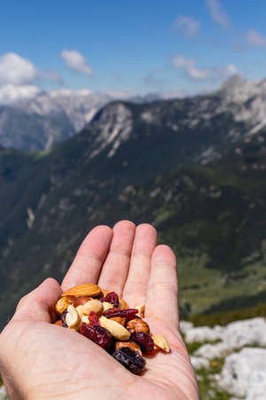 Hand holding a healthy snack on the top of the mountain after climbing. Consisting of different nuts and dried fruit, with beautiful background of mountain and forest in the summer.の写真素材