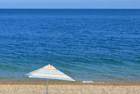 A Colourful Umbrella on a pebbled beach overlooking the oceanの写真素材