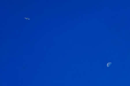 Fly Me to the Moon. A Plane is flying against a backdrop of the Moon in the vastness of a blue sky