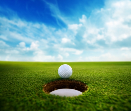 Golf ball about to fall into the cup at sunsetの写真素材
