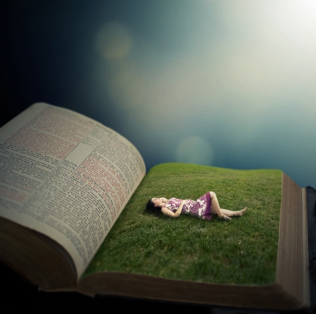 Woman laying on the pages of a Bible in a grassy field.の写真素材