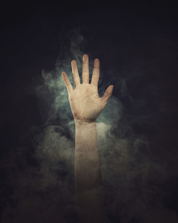 A hand reaches out in the black background from the smoke.の写真素材