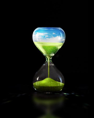 An hourglass on a black background with a green meadow falling apart.の写真素材