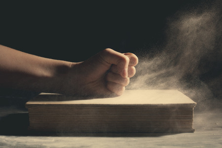 A fist pounding down on an old book with dust flying around.の写真素材