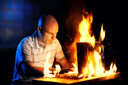 A man uses a laptop while it is engulfed in flames.の写真素材