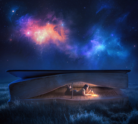 A woman reads a large Bible at night under the starsの写真素材