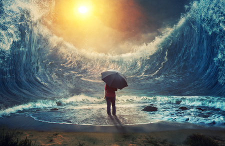 A woman surrounded by large waves and holding an umbrella.の写真素材