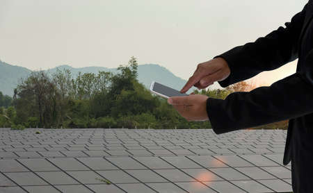 Man using a smartphone controlled  a solar panel with sky and mountains background Concept of natural energy technology.の写真素材
