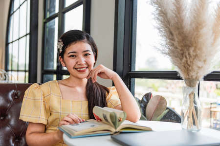 Girl is reading book beside window.