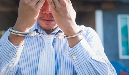 Sad businessman in handcuffs hiding his face.