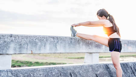 Asian woman doing warm-up exercises and stretching before running in the park in the morning in the...