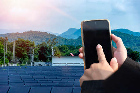 A young woman's hand uses a smartphone to monitor the electricity consumption control. Sustainable renewable energy storage station.の写真素材