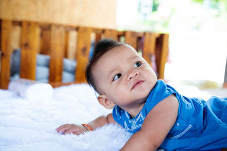A beautiful 6 month old baby with big eyes lies on the bed.