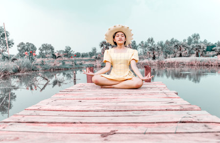 Woman practicing yoga and meditating in lotus position on wooden bridge.の写真素材