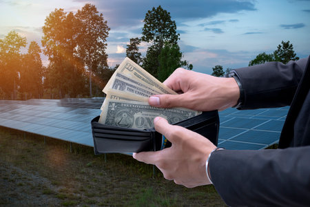 hand holding dollar bills that look out of a wallet on a background of solar panels. saves money....