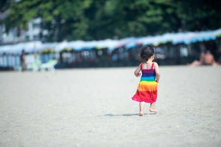 Girl playing on the beach on summer vacation, child in nature with beautiful sea, sand and blue sky, happy child on vacation by the sea, running in the water.の写真素材