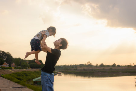 Silhouette of a mother holding up her young baby in front of a sunset.の写真素材