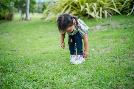 Asian girl bends down to put on shoes by herself in the backyard while doing mom and dad family vacation activities.の写真素材