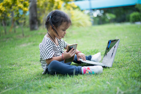 Happy asian family picnic. Daughters playing mobile phones and laptops having fun together while sitting alone on sunny day.の写真素材