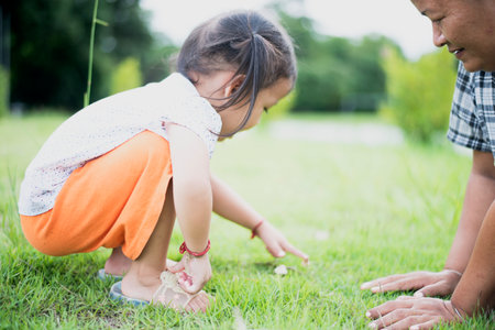 Cute Asian little girl sits on the grass in the park playing with mom.の写真素材
