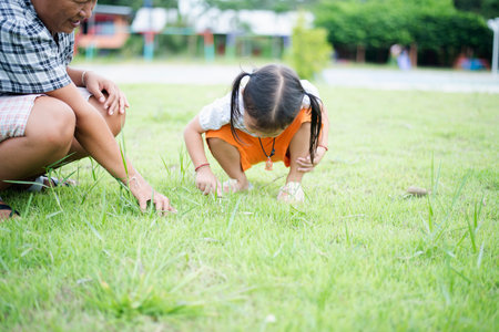 Cute Asian little girl sits on the grass in the park playing with mom.の写真素材