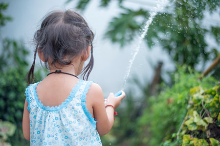 A young girl sprays water on the plants with a hose.の写真素材