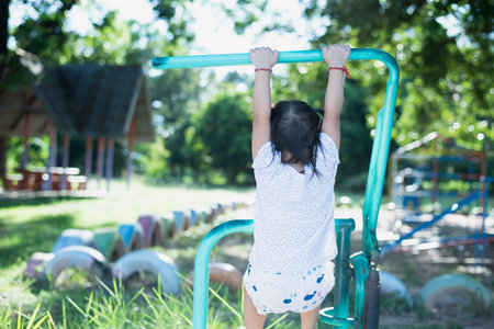 Asian girl playing on the playground with a trapeze Enthusiastic child hanging on the bar with two hands Children exercising.の写真素材