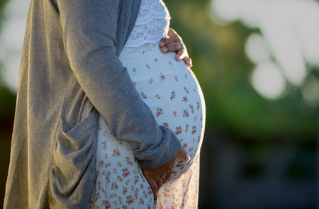 Side view close-up of pregnant woman touching her belly. Pregnancy health & wellbeing concept.