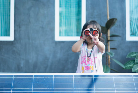 Happy Asian girl admiring solar panels with binoculars recently installed at home.の写真素材