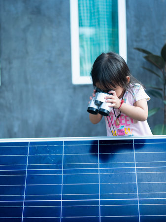 Happy Asian girl admiring solar panels with binoculars recently installed at home.の写真素材