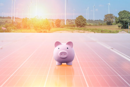 A pink piggy bank is placed on a solar panel, symbolizing savings and investment in renewable energy. Financial planning concept.の写真素材
