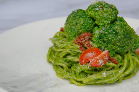 Spaghetti with pesto sauce and vegetables on a white plate.