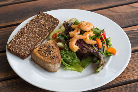 Tuna Steak and vegetable salad with shrimps and breadの写真素材