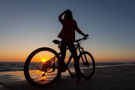 Silhouette of girl with bicycle enjoying the seascapeの写真素材